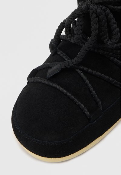 Botte en suède noire avec un bout rond, ornée de lacets noirs épais et d'un col rembourré, contrastée par une semelle en caoutchouc beige clair.