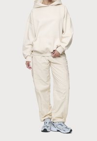 Beige hoodie med en känguruficka, överdimensionerad passform och ribbade mudd; ihopkopplad med beige cargobyxor med sidofickor och elastiska muddar.