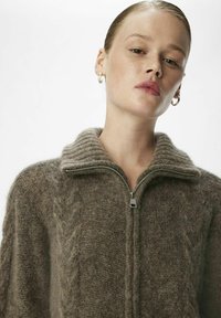 Jersey marrón texturizado con cremallera y cuello de canalé, que presenta una cremallera central y un material suave y peludo para mayor calor.