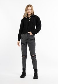 Maglione corto in maglia di cotone nera con colletto e bottoni dorati, abbinato a jeans grigi strappati e stivaletti neri con lacci.