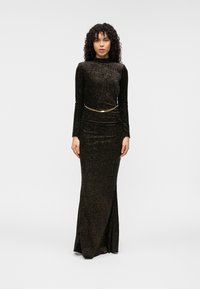 Μακρύ μαύρο φόρεμα με παγιέτες και εφαρμοστή σιλουέτα. Διαθέτει ψηλό λαιμό, μακριά μανίκια και χρυσή αλυσίδα στη μέση. Ομαλή υφή.