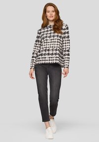 Schwarz-weiß karierter Pullover im Hahnentrittmuster mit langen Ärmeln, kombiniert mit grauer Jeans und weißen Sneakern. Glatte Stoffstruktur, lockere Passform.