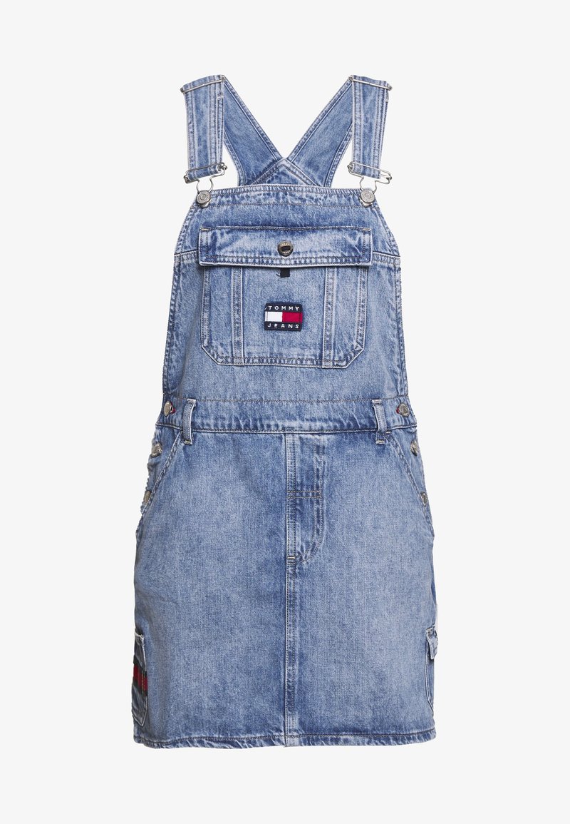 Vaaleansininen farkkuhaalarimekko, jossa on säädettävät hihnat, etutasku, brodeerattu logopatchi ja sivutaskut. Klassinen farkkukaanne.