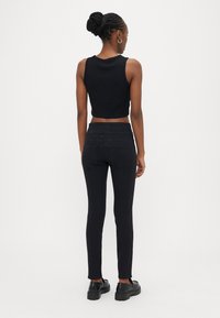 Črni kratki top brez rokavov, združen s črnimi ozkimi kavbojkami. Gladek material, oprijet kroj in preprosti šivi. Opravljeno s črnimi krepkimi �čevlji.