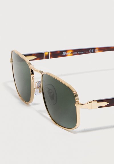 Γυαλιά ηλίου με χρυσό μεταλλικό σκελετό, τετράγωνα σκούρα πράσινα φακούς και βραχίονες με μοτίβο χελώνας, εμφανίζονται σε λευκό φόντο.