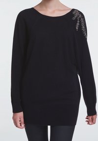 Pull en tricot noir avec une coupe décontractée, un large col et un détail décoratif en perles sur l'épaule gauche. Texture douce, manches longues.
