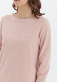 Sudadera de manga larga rosa clara con cuello redondo, que presenta un estampado texturizado de la palabra "PASSION" en un tono ligeramente más oscuro. Textura de tela suave.