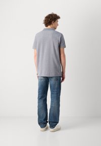 Camisa polo gris de manga corta con cuello amarillo en contraste, combinada con jeans de mezclilla azul y zapatillas blancas. Vista trasera mostrada.