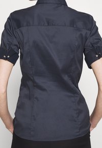 Kortärmad, figursydd skjorta i marinblå polyester, med klassisk krage, uppvikta ärmar med knapppartier och en slät textur.