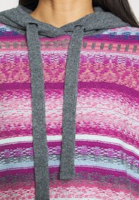 Rosa och grå stickad hoodie med dragsko, med horisontella ränder i varierande nyanser av rosa, lila och blått.