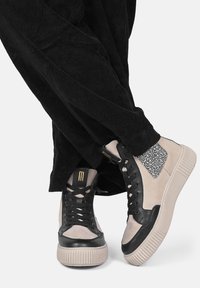 Le scarpe da ginnastica alte presentano una combinazione di pelle nera e suede beige, con un accento a stampa leopardata e dettagli in oro sul linguetta.