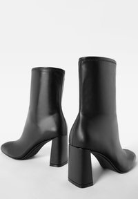 Schwarze Lederstiefeletten mit quadratischen Absätzen, glatter Textur und taillierter Passform. Betont durch minimalen Nähten am oberen Rand.