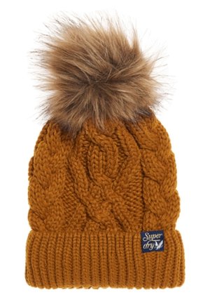 Gebreide mosterdgele muts met kabelpatronen, geribbelde boord, bruine nepbont pompon en een klein rechthoekig merkje op de boord.