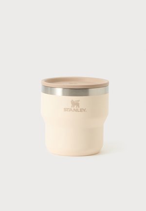 Gobelet isolant couleur crème avec couvercle beige et bord argenté, avec le logo Stanley à l’avant.