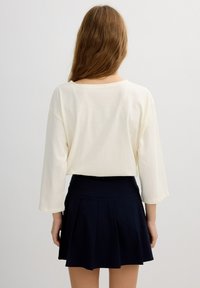 Camisa de manga larga color crema con un corte relajado, combinada con una falda mini azul marino con pliegues. Textura suave, diseño casual, sin patrones visibles.