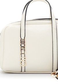 Krémová kabelka s černým lemováním, dvojitými uchy a zlatým přívěskem "CAFE NOIR" visícím z jednoho ucha.