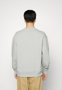 Felpa grigia realizzata in tessuto morbido, con colletto a girocollo, spalle scese e polsini a coste, indossata con pantaloni beige.