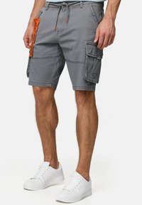 Szare szorty cargo z pomarańczowym sznurkiem, z wieloma kieszeniami i detalami wykończenia. Połączone z białymi sneakersami.