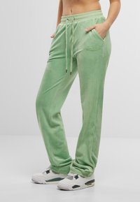 Grønne velour joggebukser med elastisk midjebånd, justerbar snøring, sidelommer og brodert merke på låret.