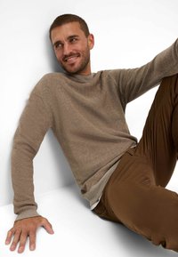 Light brown ribbed sweater with a round neckline, long sleeves, and textured fabric, paired with brown straight-leg pants.