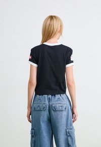 Černé zkrácené tričko s bílým lemováním a nášivkou na levém rukávu, kombinované s volnými džínovými cargo kalhotami se zadními kapsami.