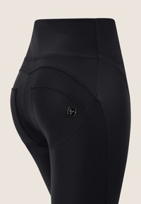 Leggings neri a vita alta con cuciture curve, un design elegante, una piccola etichetta con marchio sulla tasca posteriore e un tessuto liscio e elastico.