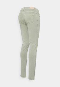 Jeans verde-claro, ajustados, com uma textura suave, apresentando bolsos traseiros e uma pequena etiqueta bege na cintura.