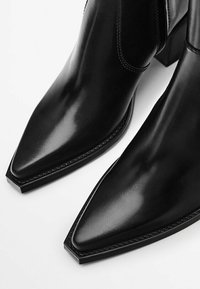 Stivali neri in pelle fino alla caviglia con punta affusolata, design elegante, texture liscia, tacco a blocco moderato e dettagli di cucitura sottili lungo i bordi.