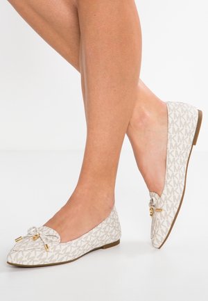Ben iført beige designer loafers med monogrammønster, sløjfe og guldfarvede accenter, vist på hvid sømløs baggrund.