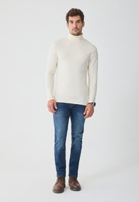 Top cu guler înalt dintr-un material moale, purtat cu blugi de denim albaștri și cizme maro cu șireturi. Design simplu, siluetă ajustată.