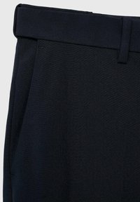 Pantalones azul marino confeccionados en tejido texturizado, con una cintura plana y bolsillos laterales para un aspecto ajustado. Diseño minimalista sin adornos.