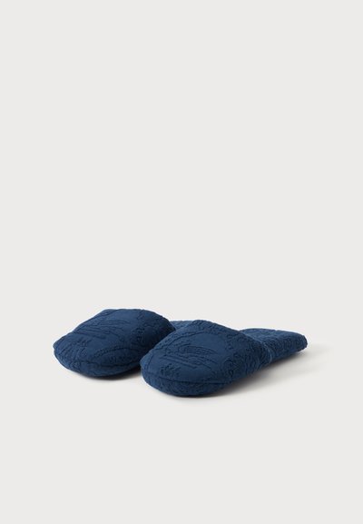 Paire de chaussons en tissu texturé bleu foncé, sans lacets, avec bouts fermés, présentée sur un fond clair uni.