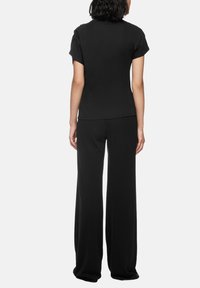 Black short-sleeve top paired with loose-fitting black pants. Fabric appears smooth with a relaxed silhouette and minimal detailing.