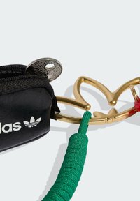 Zwart etuitje met zilveren beslag, groene opgerolde band en gouden metalen accessoire in de vorm van een bloem. Voorzien van een wit logo.