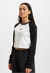 Black long sleeves with a white cropped body featuring a red logo in the center. Cotton material, relaxed fit, and ribbed neckline.