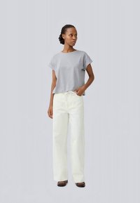 Tricou gri scurt cu mâneci scurte, asociat cu pantaloni albi largi. Ambele articole sunt simple ca design și textură a țesăturii.