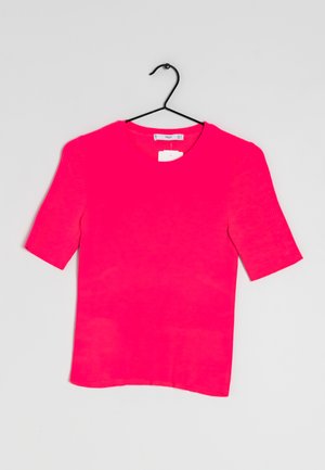 Rosa ribbet kortærmet top med rund halsudskæring, glat tekstur og et mærke vedhæftet, hængende fra en sort krog mod en lys baggrund.