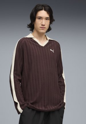 Chemise manches longues bordeaux avec texture côtelée verticale, col crème et bandes latérales. Présente un petit logo Puma blanc sur la poitrine.