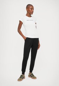 Hvid kortærmet t-shirt med sort "ARMANI EXCHANGE" tekst, parret med sorte joggers og olivengrønne sneakers med sorte striber.