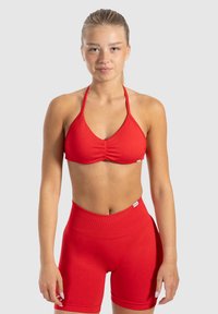 Top de bikini rojo con tirantes al cuello y centro fruncido, acompañado de pantalones cortos de talle alto a juego, fabricados con un tejido liso y elástico. Diseño sencillo, sin patrones.