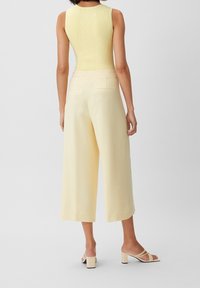 Żółty prążkowany top bez rękawów w połączeniu z szerokimi, jasnżółtymi spodniami. Spodnie mają tylne kieszenie i gładką fakturę.