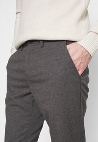Gray tailored trousers made of textured fabric with a straight leg design, featuring side pockets and a mid-rise waist, paired with a knit sweater.