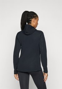 Schwarzer Hoodie mit langen Ärmeln und hohem Kragen, aus strukturiertem Material und mit Flachnähten, getragen mit engen Leggings.