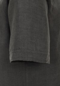 Košile s krátkými rukávy vyrobená z tmavě šedé lněné tkaniny. Má čistý lem a hladký, mírně texturovaný povrch.