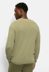 Olivgrüner Strickpullover mit strukturierter, gerippter Optik, rundem Ausschnitt und enganliegenden Bündchen. Mit kleinem Logo-Akzent am Saum.