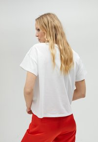 Bílý krátký rukáv tričko s uvolněným střihem, kulatým výstřihem a hladkou texturou, v kombinaci s červenými kalhotami.