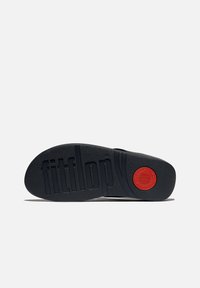 Sole in gomma nera con "fitflop" in rilievo, caratterizzata da un accento rosso rotondo e sezioni di grip testurizzate. Forma curvata per supporto ergonomico.