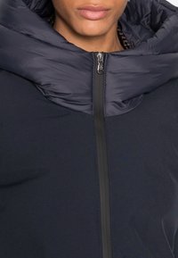 Námořnická pufovaná bunda s vysokým límcem, se zipem vpředu a hladkou, jemnou texturou. Teplý, izolační materiál se sportovním designem.