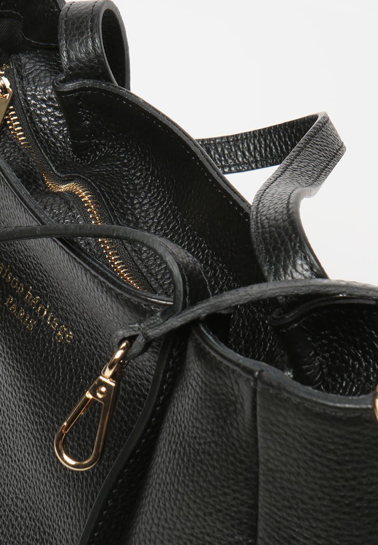 Schwarze Lederhandtasche mit strukturierter Oberfläche, goldener Reißverschluss und metallischen Hardware-Akzenten. Offene Oberseite, die die Innenfächer offenbart.