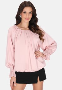 Rosa Satinbluse mit Falten, Ballonärmeln und gesmockten Bündchen, kombiniert mit einem schwarzen Minirock mit seitlichem Schlitz.